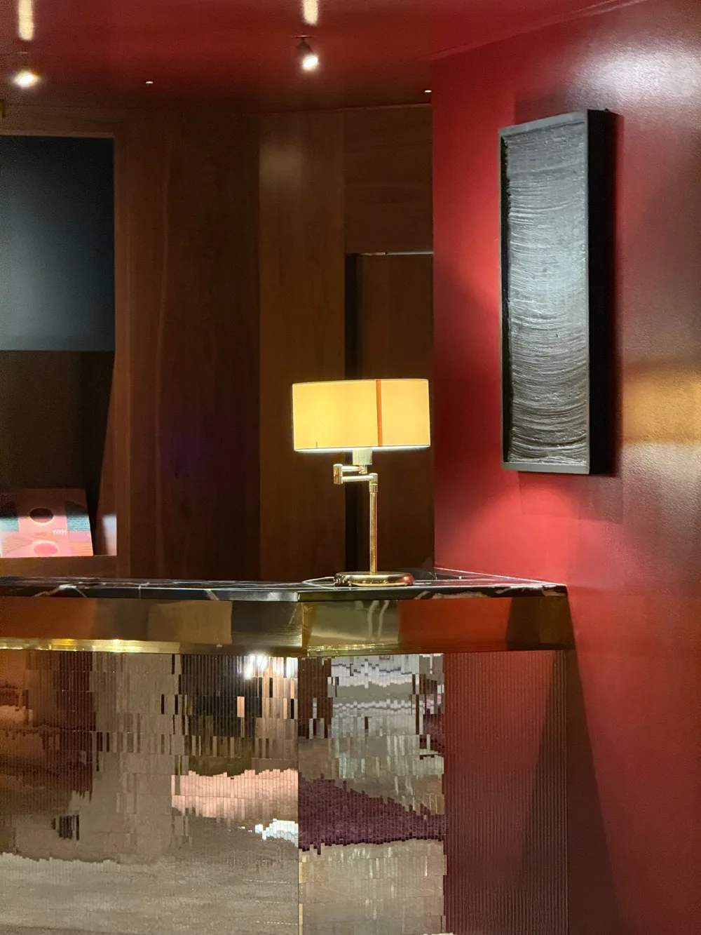 A brass table lamp on a dark marble console against a deep red wall in a 1960s hotel.
